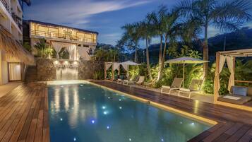 A pool area with a wooden deck, lounge chairs, and a waterfall feature.