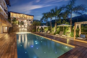 A pool area with a wooden deck, lounge chairs, and a waterfall feature. - Casa Bocana Huatulco (Santa María Huatulco)