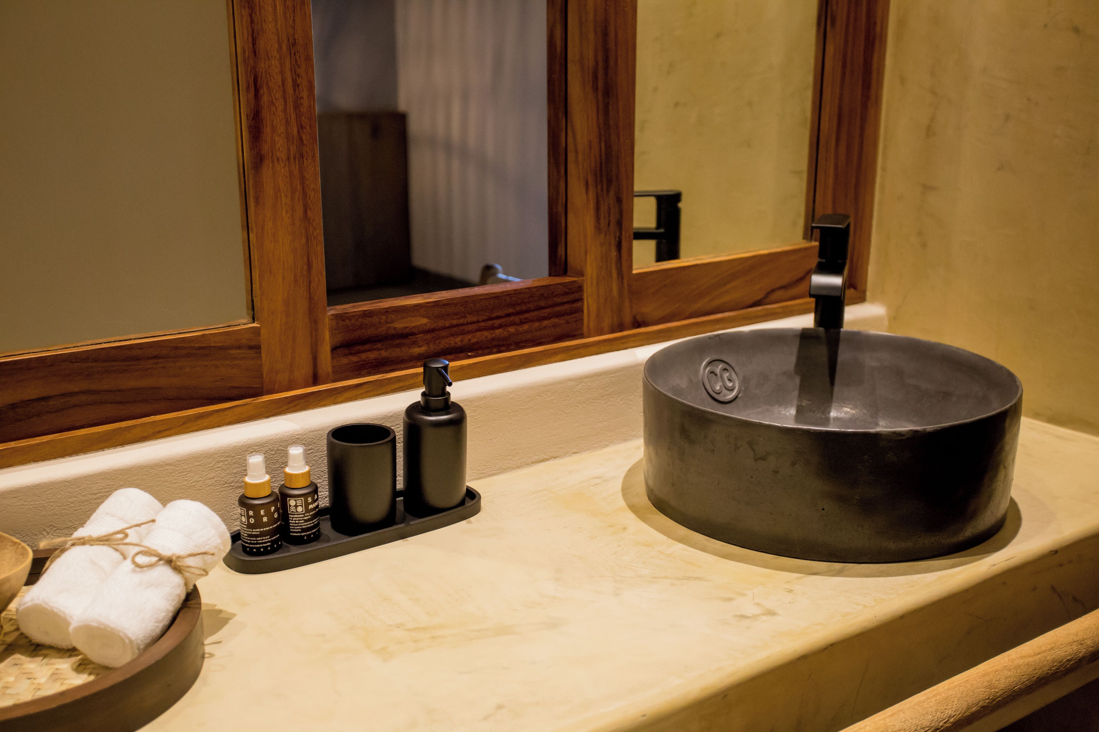 A bathroom with a wooden-framed mirror, a sink with a black basin, and toiletries on the countertop.