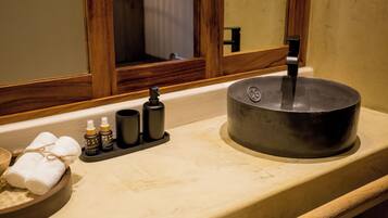 A bathroom with a wooden-framed mirror, a sink with a black basin, and toiletries on the countertop.