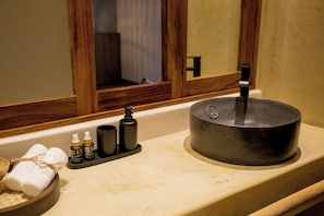 Un bany amb un mirall de fusta, un lavabo amb una pila negra i productes de tocador a la superfície.