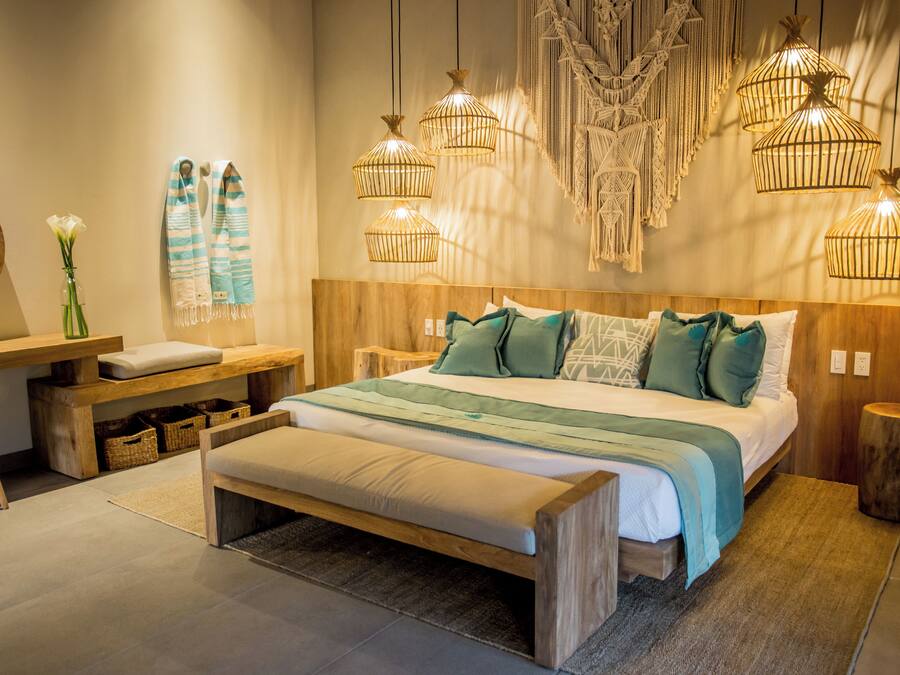 A modern bedroom with a wooden bed, a bench, a bedside table, and a hanging light fixture.