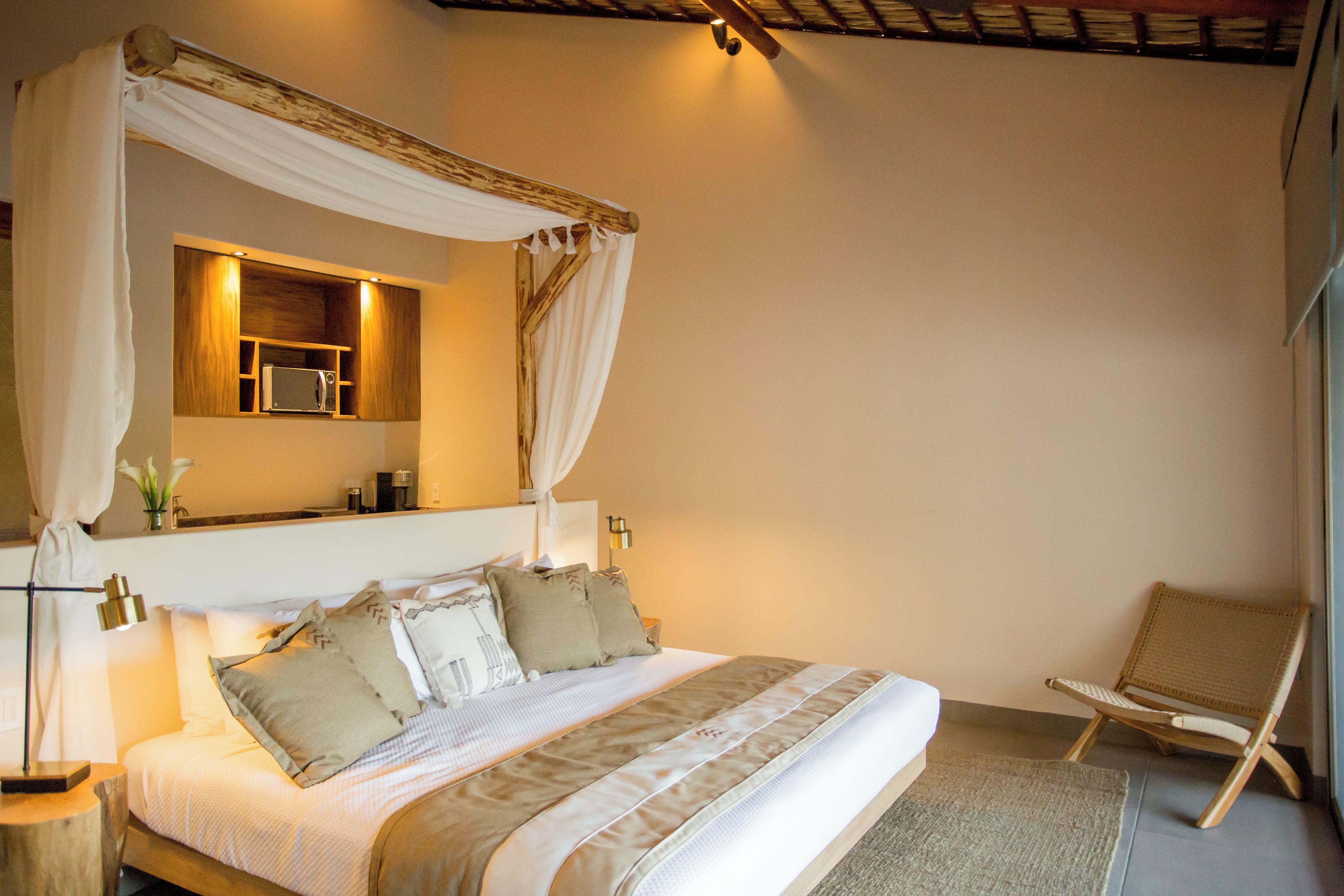 A bedroom with a canopy bed, bedside table, lamp, and a chair.
