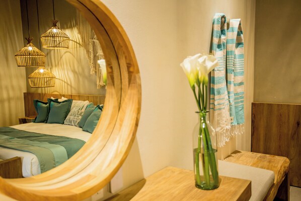 A bedroom with a wooden headboard, a bed with green bedding, a wooden nightstand, a mirror, a vase with white flowers, and a blue and white striped towel. - Casa Bocana Huatulco (Santa María Huatulco)