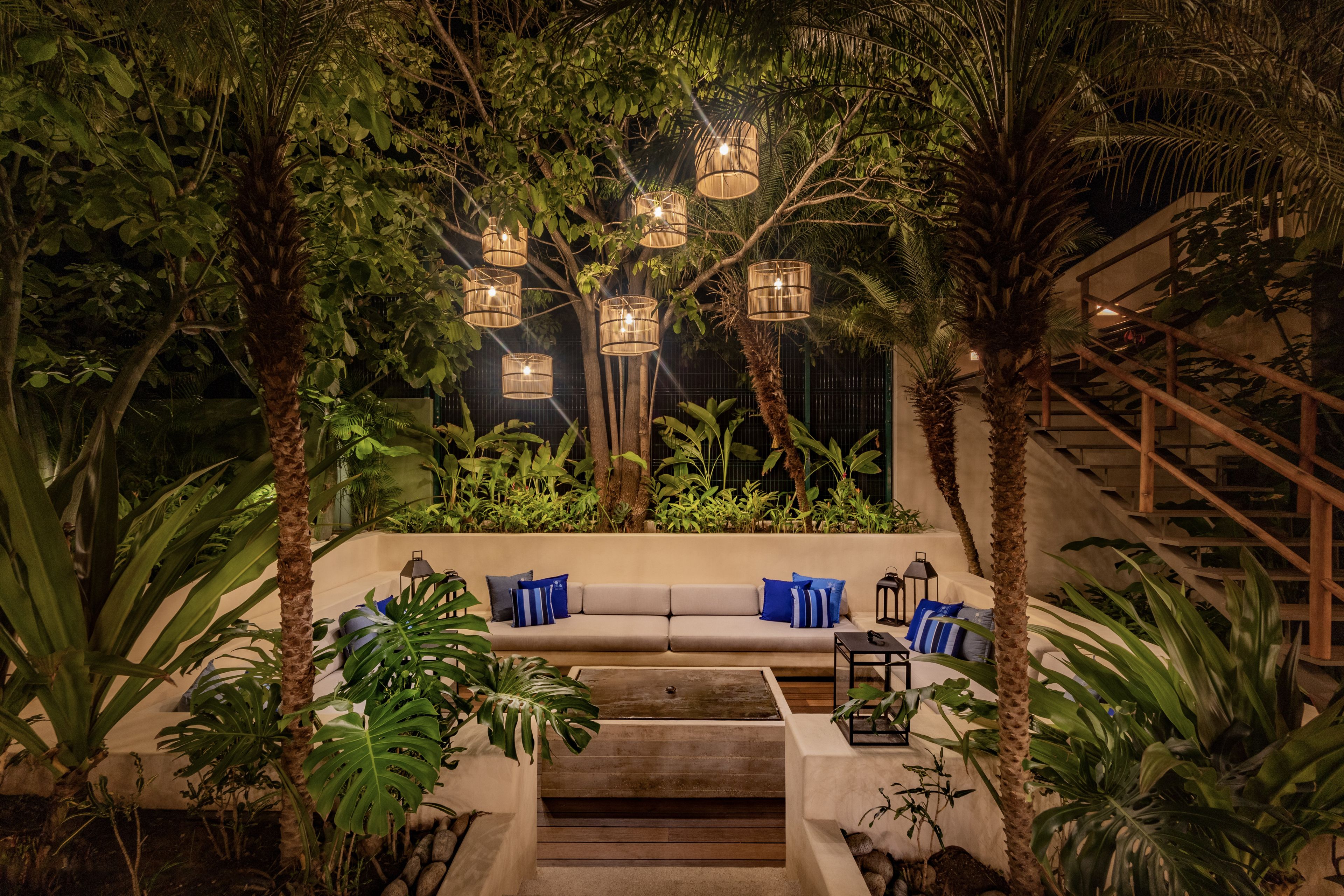 A cozy outdoor seating area with a sofa and cushions, surrounded by lush greenery and palm trees.