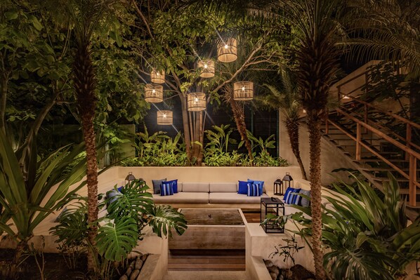 A cozy outdoor seating area with a sofa and cushions, surrounded by lush greenery and palm trees. - Casa Bocana Huatulco (Santa María Huatulco)
