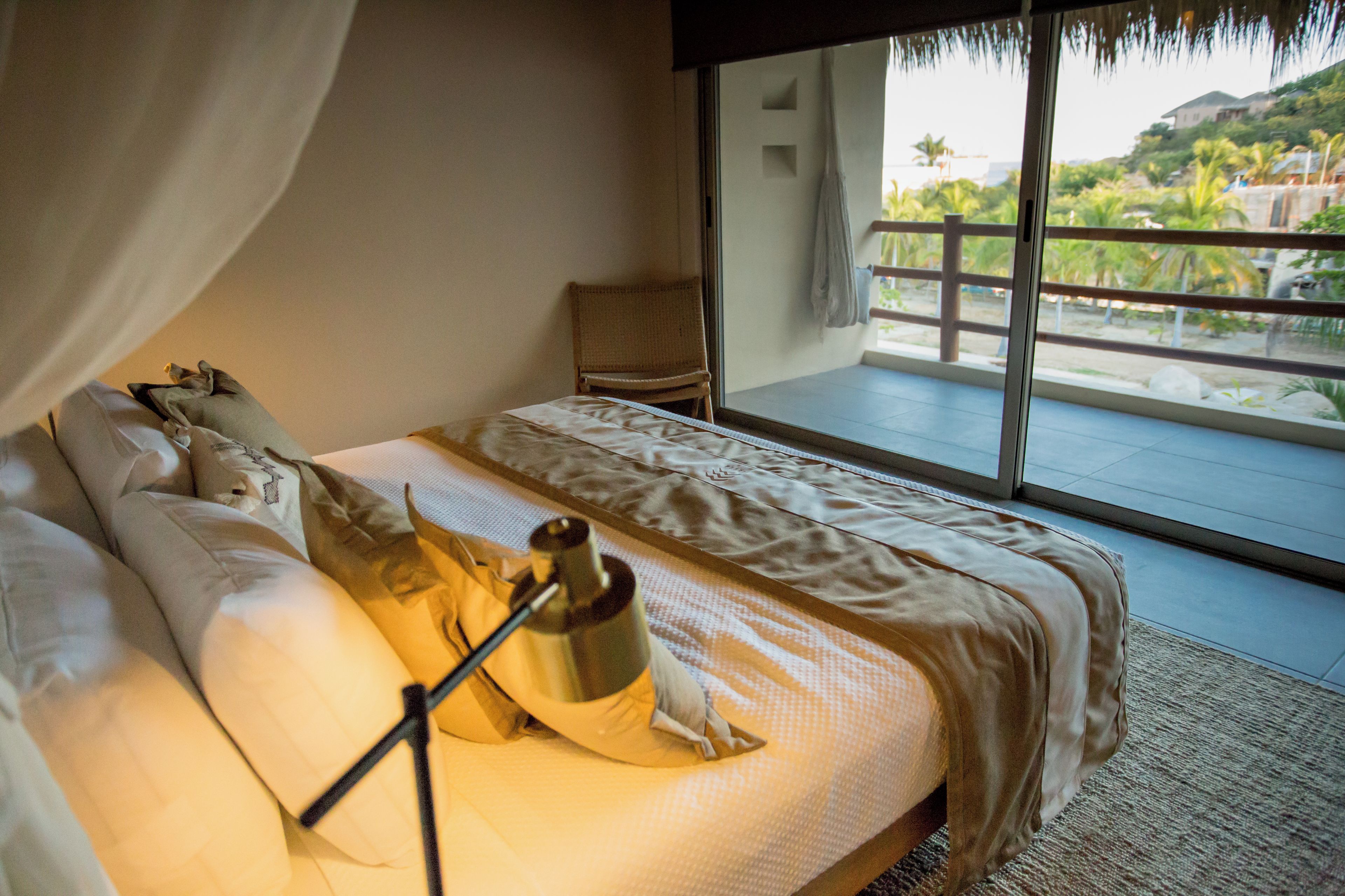 A bedroom with a large bed, a nightstand, and a view of a balcony with a railing.