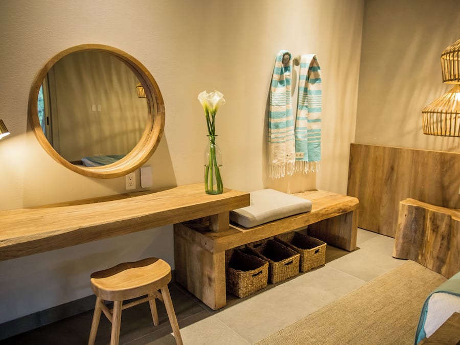 A modern bathroom with a wooden vanity, a round mirror, a vase with flowers, a towel rack, and a hanging light fixture.