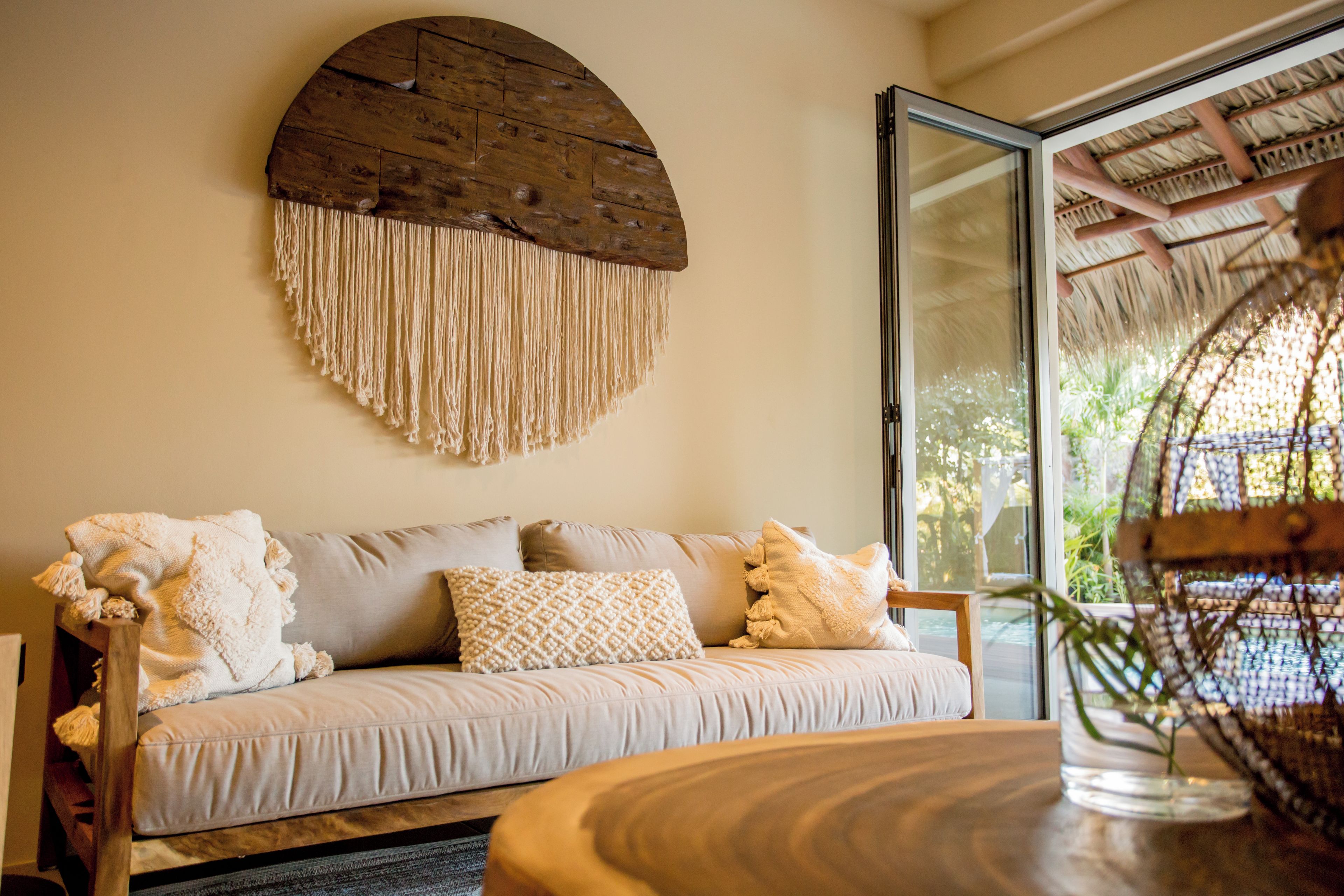 Una sala de estar acogedora con un sofá, un adorno de pared de madera y un ventanal que da a un espacio exterior.