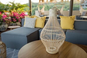 Una lámpara de mimbre sobre una mesa de madera en un área de estar exterior moderna, con un sofá y cojines.