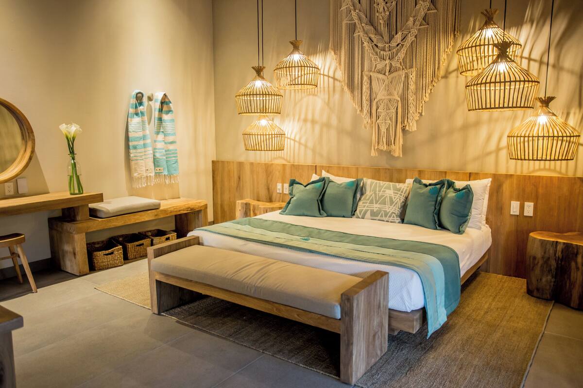 A modern bedroom with a wooden bed, bedside tables, a bench, and hanging light fixtures.