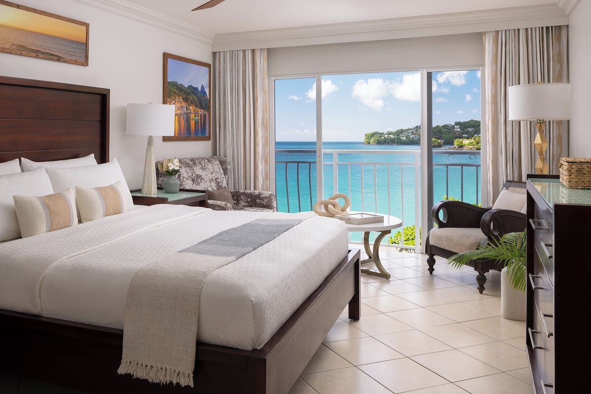 A spacious bedroom with a large bed, a view of the sea, and a balcony with a chair.