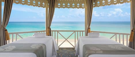 A room with two beds, a view of the ocean, and a balcony with a railing.