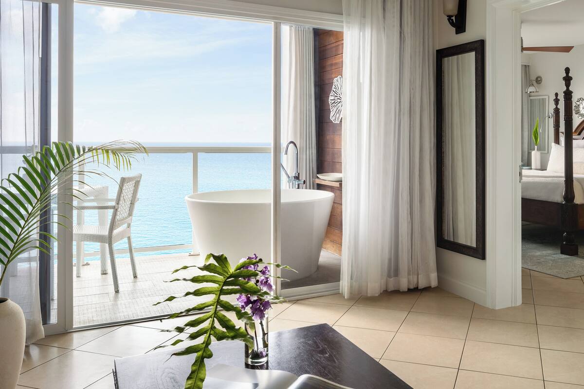 A hotel room with a balcony, a bathtub, a bathroom, and a bed.