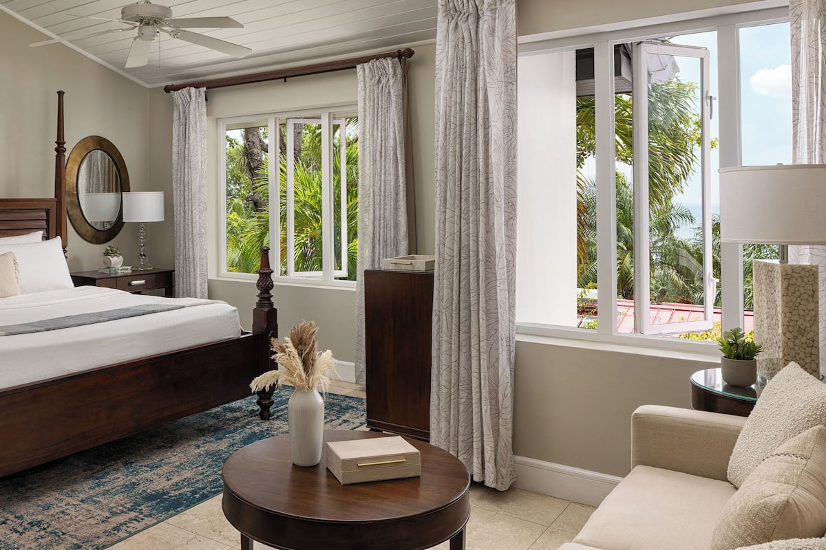 A hotel room with a large bed, a round wooden table, a nightstand, a mirror, and a view of the outdoors.