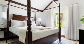 A four-poster bed with a wooden headboard, a bedside table with a lamp, and a view of greenery through the window. - Sandals Regency La Toc (Castries)