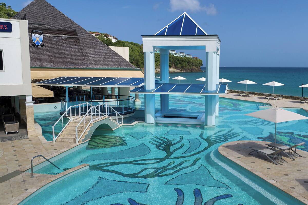 A pool with a blue and white structure, lounge chairs, and umbrellas.