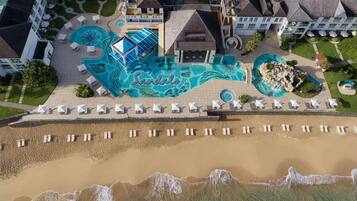 Vista aérea de un resort con varias piscinas, una zona de playa con tumbonas y un jardín ajardinado.