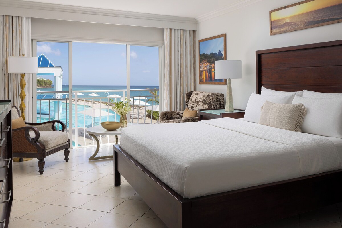 Une chambre spacieuse avec un grand lit, une vue sur l’océan et un balcon avec une piscine.