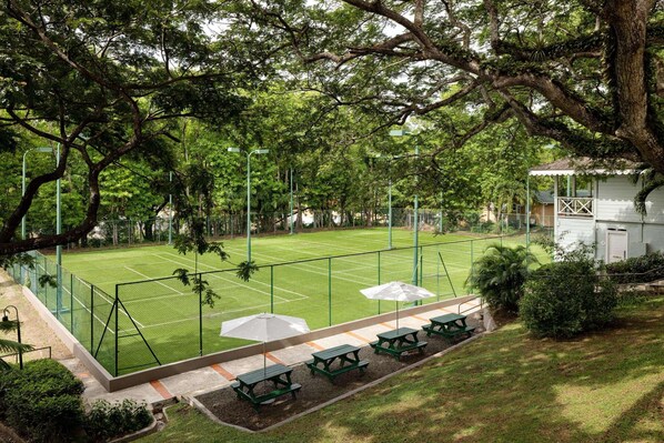 A tennis court with a green fence, picnic tables, and umbrellas. - Sandals Regency La Toc (Castries)