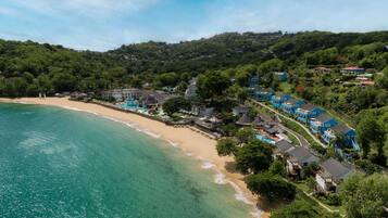 Un complejo turístico frente a la playa, con villas, piscina y abundante vegetación.
