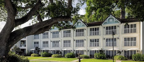 Um hotel de vários andares com fachada simétrica, janelas amplas e um jardim bem cuidado com uma fonte central.