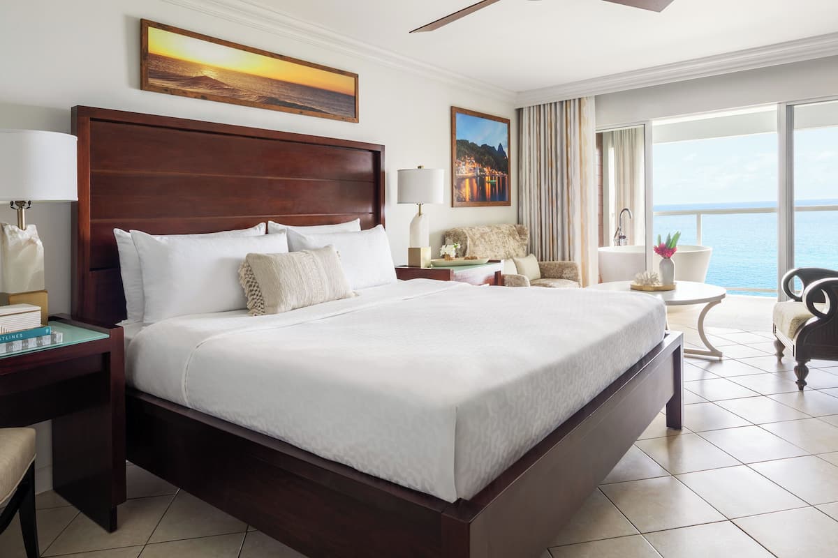 A hotel room with a large bed, a desk, a chair, and a view of the sea.