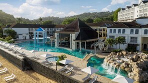 Ein Resort mit einem großen Schwimmbad, einem Wasserfall und einem Strandbereich mit Liegestühlen.