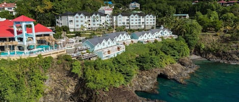 A coastal resort with multiple buildings, a swimming pool, and rocky cliffs.