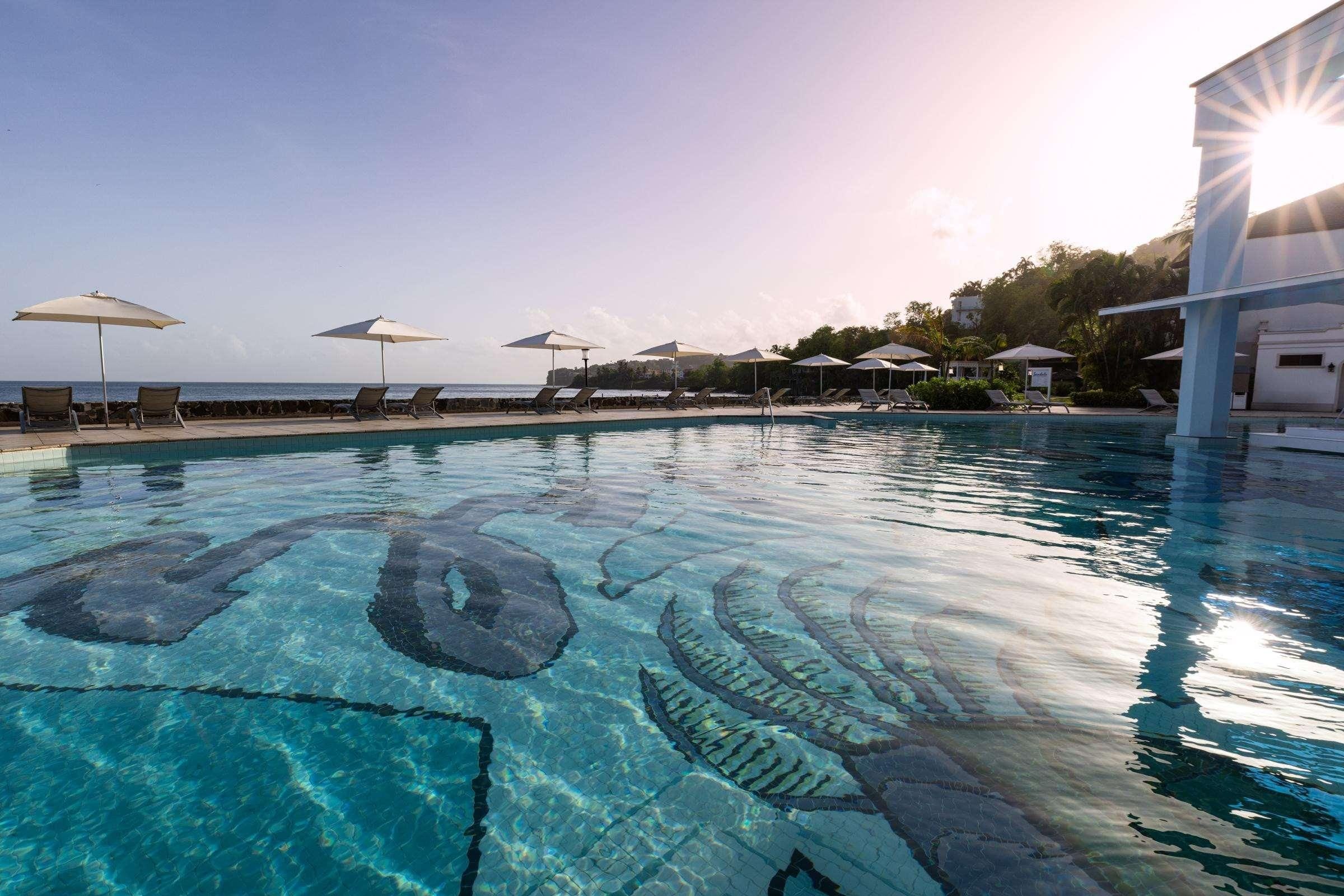 A pool with clear water and a sun reflection, surrounded by lounge chairs and umbrellas.