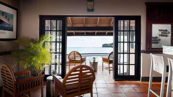 A room with a view of the sea, wooden chairs, a small table, and a potted plant.