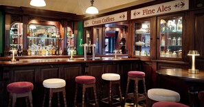 Ein Barbereich mit Hockern, einer Theke mit Flaschen sowie Schildern für 'Cream Coffees' und 'Fine Ales'.