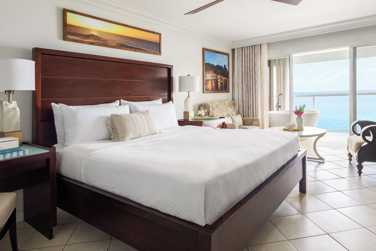 Une chambre d’hôtel avec un grand lit, un bureau, une chaise et une vue sur la mer.