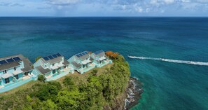 Una proprietà costiera con diverse case azzurre, dotate di pannelli solari, una piscina e vista sull'oceano.