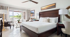 A spacious hotel room with a large bed, a balcony with a view, a desk, and a chair. - Sandals Regency La Toc (Castries)