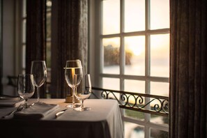 A table set for dining with wine glasses and cutlery, overlooking a scenic view through a window with a view of a body of water. - Sandals Regency La Toc (Castries)