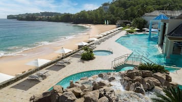 Un resort con playa, piscina con cascada y vista al océano.