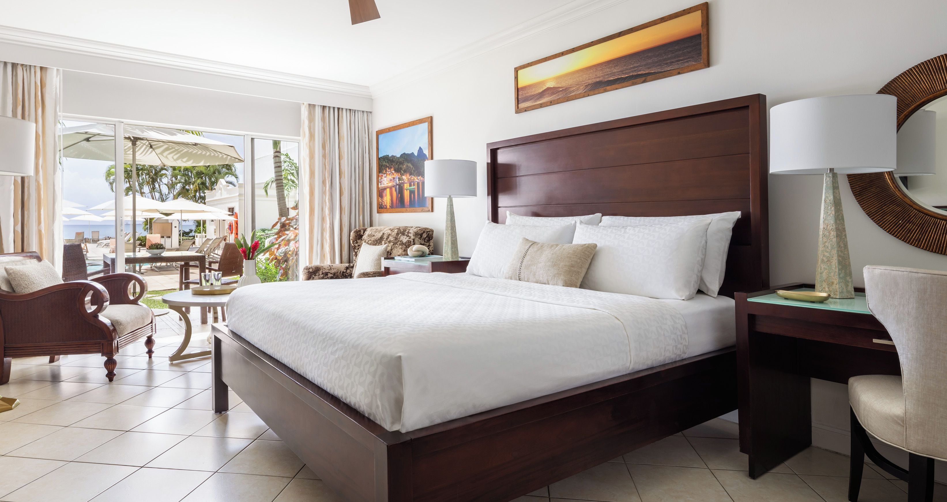 Un dormitorio amplio con una cama grande, un escritorio y una silla. Se aprecia vista al exterior a través de ventanas amplias.
