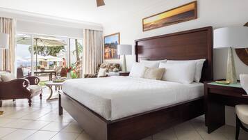 Un dormitorio amplio con una cama grande, un escritorio y una silla. Se aprecia vista al exterior a través de ventanas amplias.
