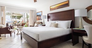 A spacious bedroom with a large bed, a desk, and a chair. There is a view of the outdoors through large windows.