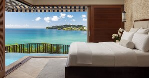 Une chambre avec un grand lit, une vue sur une mer turquoise et une balustrade en bois.