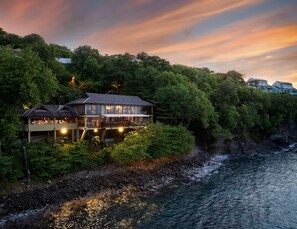 A coastal building with multiple levels, surrounded by dense greenery and overlooking a rocky shoreline. - Sandals Regency La Toc (Castries)