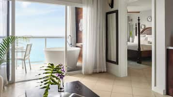 Habitación de hotel con balcón, bañera grande, cama y vista al mar.
