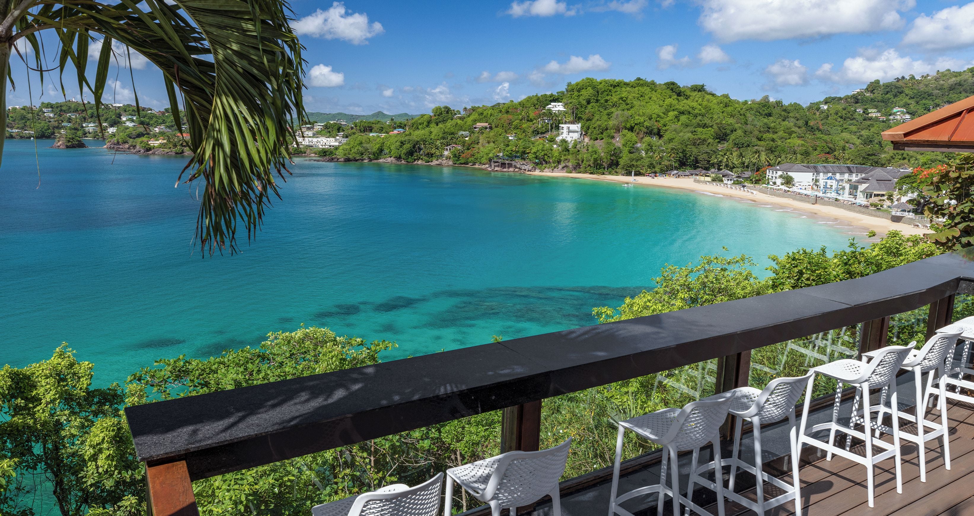 A deck with white plastic chairs overlooking a turquoise sea and a beach.