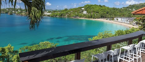Um terraço com cadeiras de plástico branco com vista para um mar azul-turquesa e uma praia.