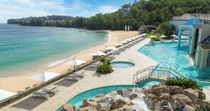 Ett semesterparadis med en strand, en pool med ett vattenfall och en lusthus.
