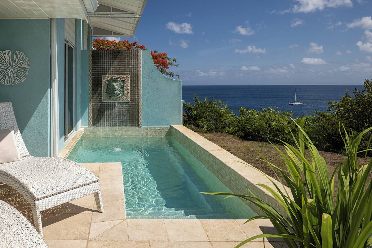 A pool area with a view of the ocean, a covered seating area, and a decorative wall.