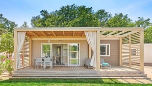 A modern outdoor patio area with a wooden deck, a dining table with chairs, and a seating area with a cushioned chair.