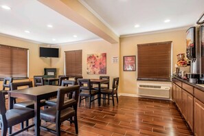 Habitación de hotel con zona de comedor, televisión de pantalla plana, un cuadro, un cartel y kitchenette.