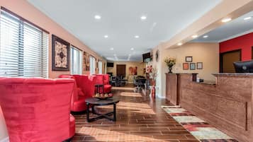 Un vestíbulo de hotel con asientos rojos, una recepción y un suelo de baldosas.